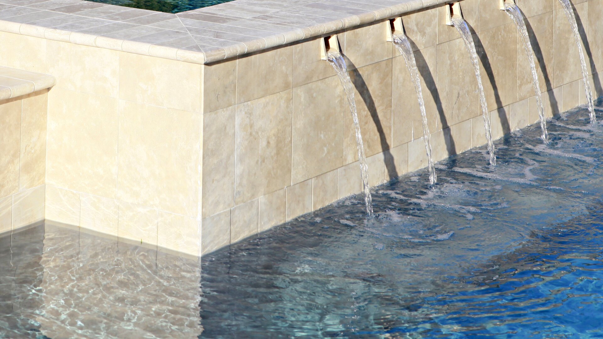 Light-coloured natural stone pool with water inlets.