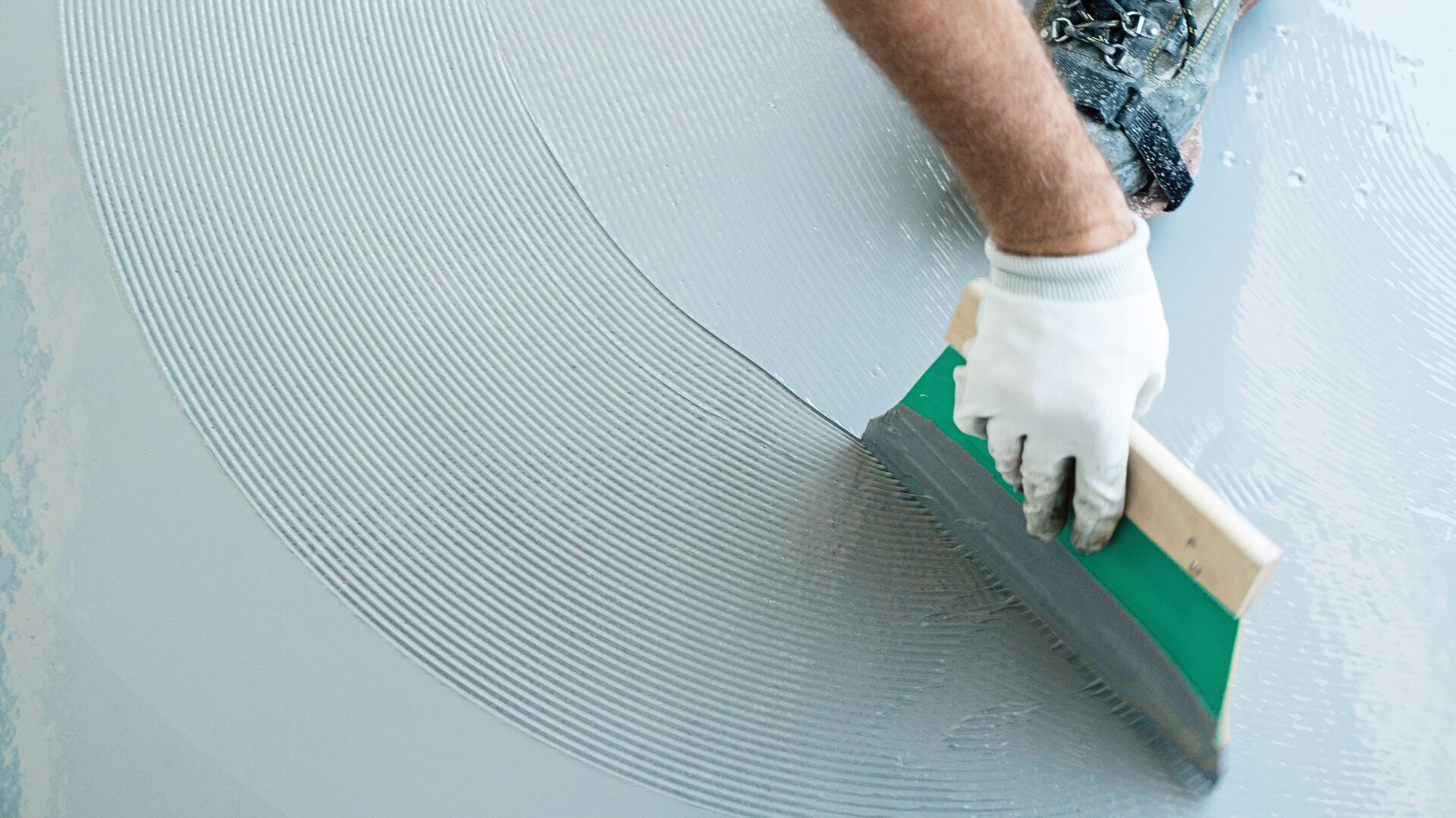 Hand of a Ramsauer employee using a smoothing tool to spread sealing slurry evenly over a surface.